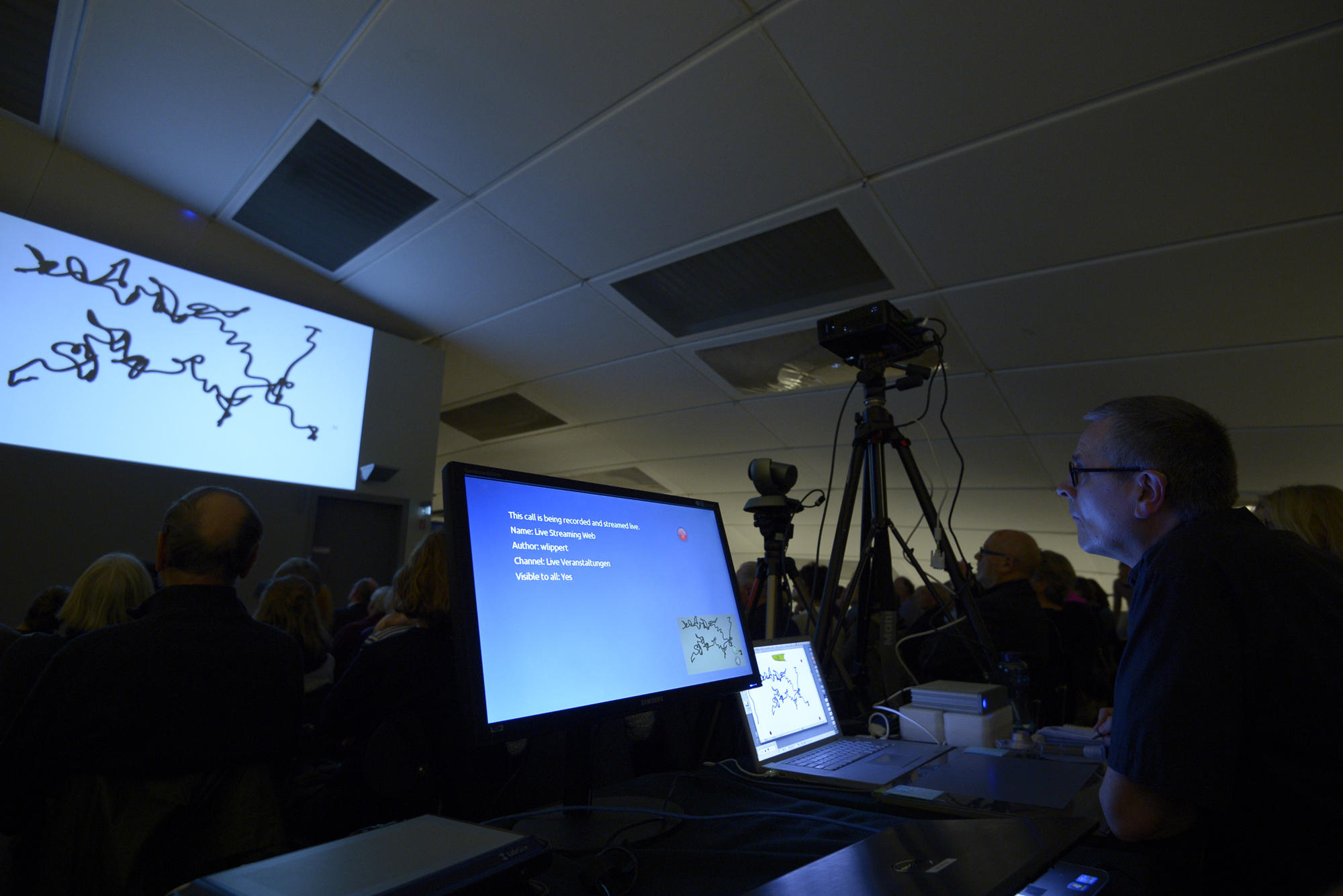 Skripturale Methode: Alex Malik zeichnet Kringel, Kurven und Linien, die über einen Beamer an die Wand geworfen werden.