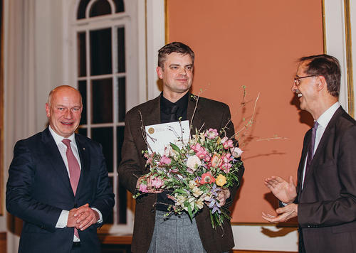Preisträger Matthias Nawrat nimmt Blumen in Empfang, Berlins Regierender Bürgermeister Kai Wegner (links) und Hans Gerhard Hannesen, Vorstandsvorsitzender der Stiftung Preußische Seehandlung, gratulieren.
