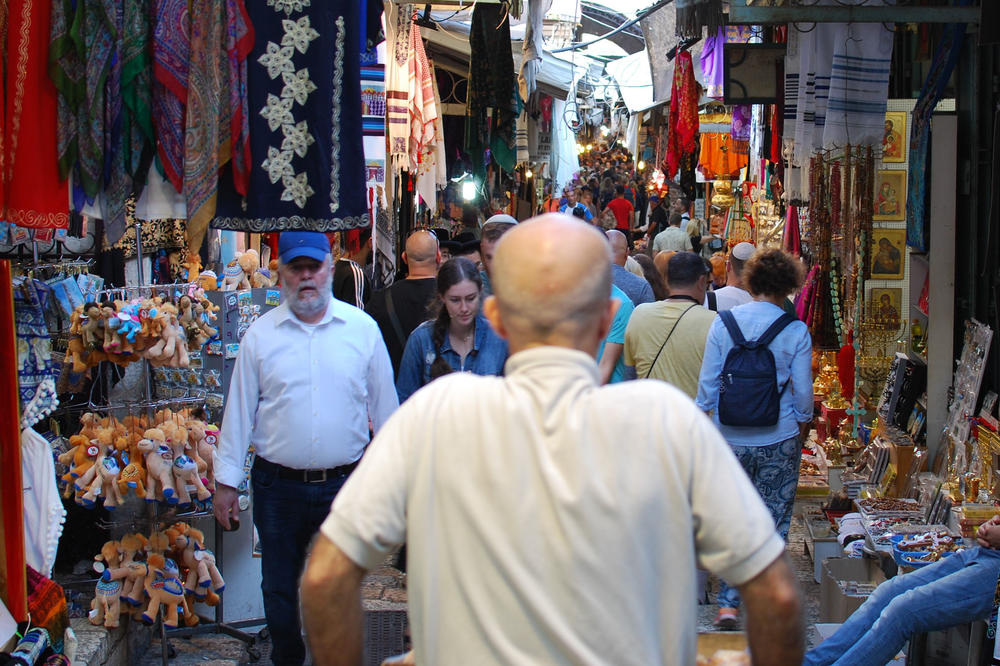A man is trying to push a cart full of bread through the crowded streets in Jerusalem’s Old City. Tourists, believers, and small shops are everywhere.