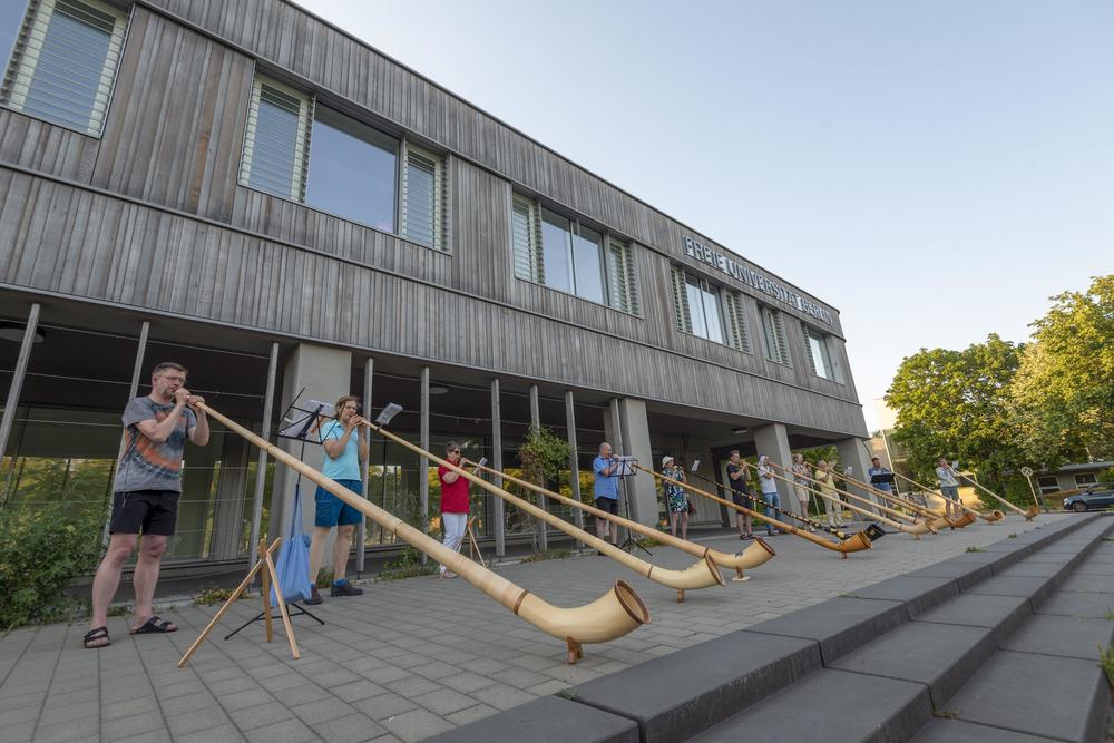 Mitglieder des Vereins „Alphorn.Berlin“ proben vor der Holzlaube der Freien Universität.