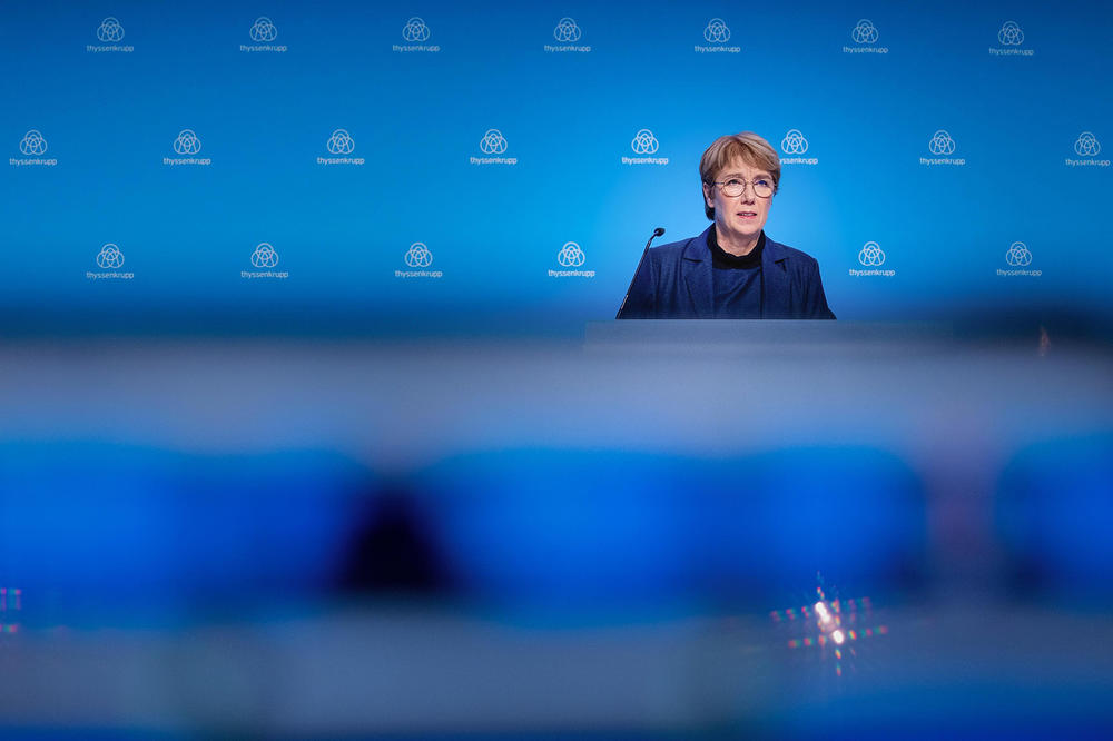 Martina Merz auf dem Podium mit Mikrofon vor blauem Hintergrund
