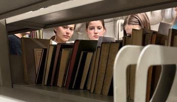 Die Schülerinnen wählen am Regal Bücher für die Recherche aus.