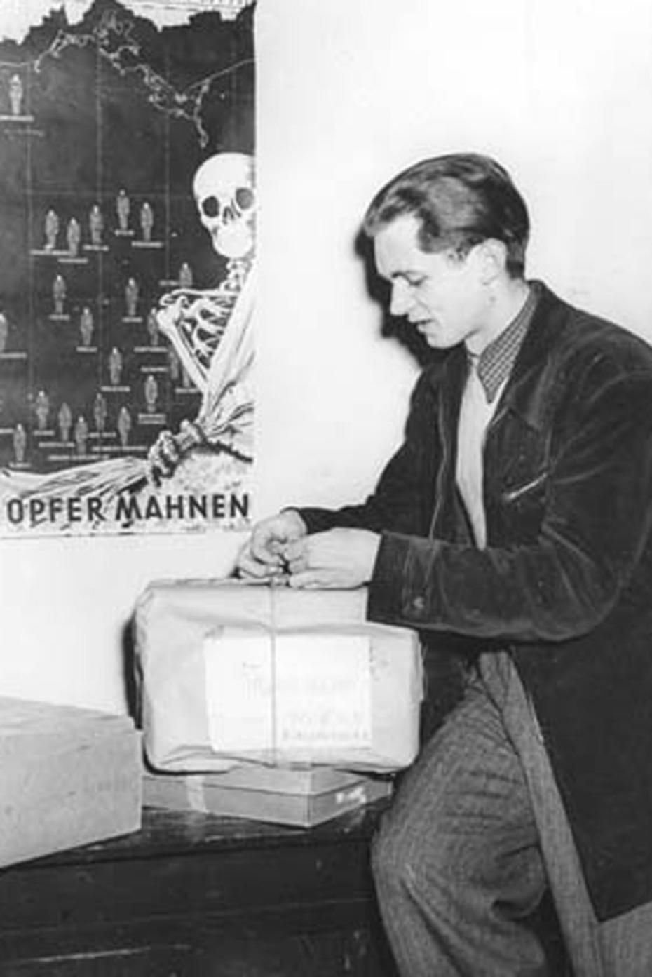 Ein Student bei der Versendung von Lebensmittelpaketen an Studierende der Ostzone. Im Hintergrund ein Propagandaplakat des „Befreiungskomitees für die Opfer totalitärer Willkür“, 1952.